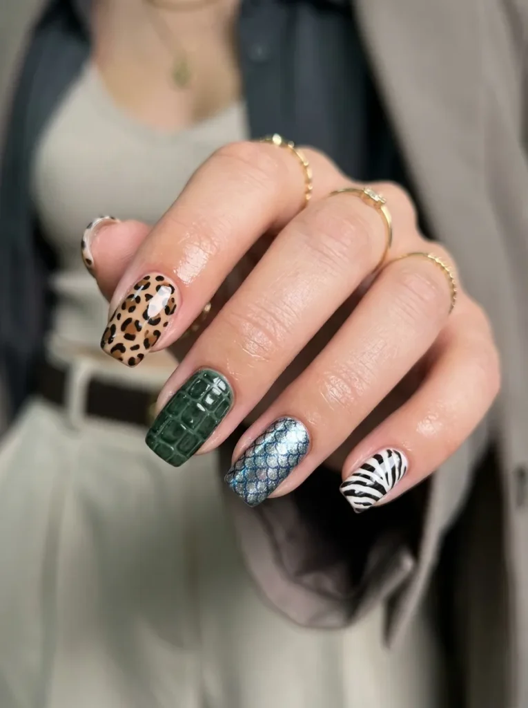 A macro close-up, high-fashion editorial photograph of a woman's perfectly manicured hand. The nails feature a bold, trendy mix-and-match animal print design: one nail showcases classic leopard spots, another has striking black and white zebra stripes, one features a dark green 3D croc-embossed texture, and another has a quirky, shimmering metallic "sardine" pattern. Flawless glossy finish, edgy and fun vibe. Softly blurred chic outfit in the background to keep the focus on the nails. Photorealistic, 8k resolution, highly detailed studio lighting.
